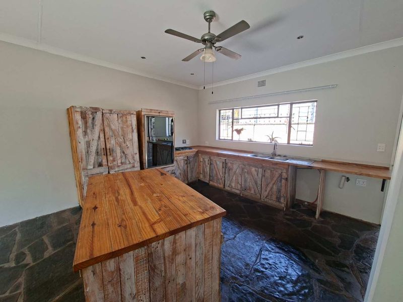 A rustic-style kitchen featuring wooden cabinetry, a central island, built-in oven, and stone flooring, offering a unique aesthetic with potential for modernization.