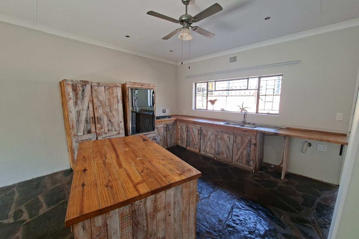 A rustic-style kitchen featuring wooden cabinetry, a central island, built-in oven, and stone flooring, offering a unique aesthetic with potential for modernization.