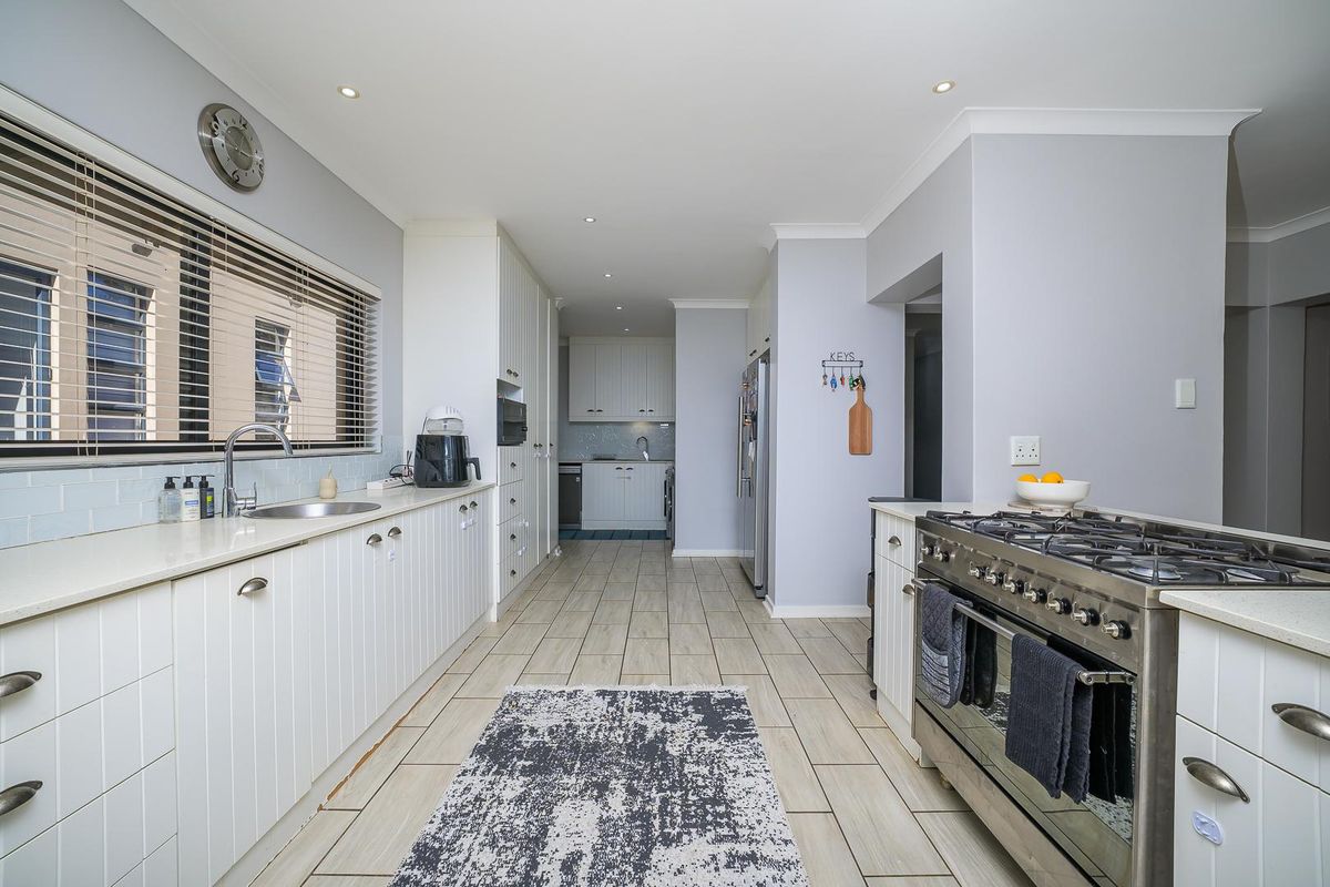 Modern kitchen featuring white cabinetry, stone countertops, a large gas range, and tiled flooring with a clean, functional layout.