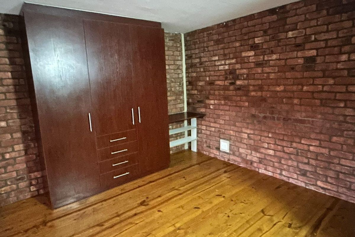 A bedroom featuring exposed brick walls, polished timber flooring, and a large built-in wooden wardrobe.