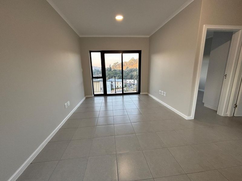 An empty, well-maintained living area featuring neutral tiled flooring, recessed lighting, and a sliding glass door leading to a balcony with scenic views.