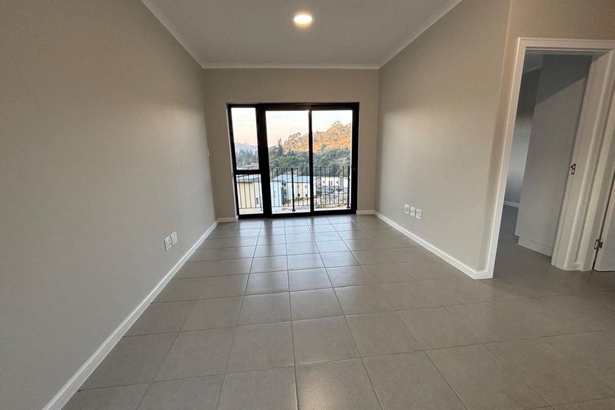 An empty, well-maintained living area featuring neutral tiled flooring, recessed lighting, and a sliding glass door leading to a balcony with scenic views.