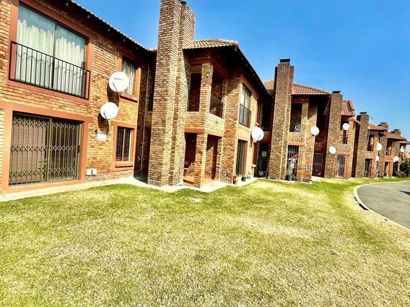 Rear view of a multi-unit cluster complex featuring face-brick architecture, prominent chimneys, tiled roofing, and shared lawn space.