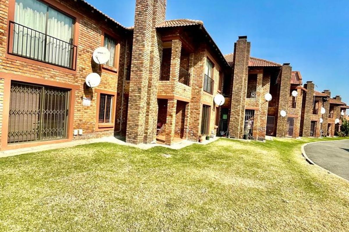 Rear view of a multi-unit cluster complex featuring face-brick architecture, prominent chimneys, tiled roofing, and shared lawn space.