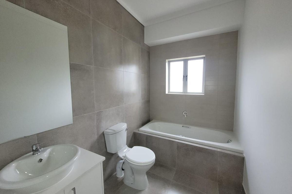 Modern bathroom featuring large format neutral wall tiles, a built-in bathtub, a vanity with a basin, and a wall-mounted mirror.