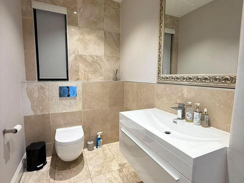 Modern bathroom featuring a floating vanity, wall-mounted toilet, and elegant travertine tiling throughout, creating a clean and contemporary aesthetic.