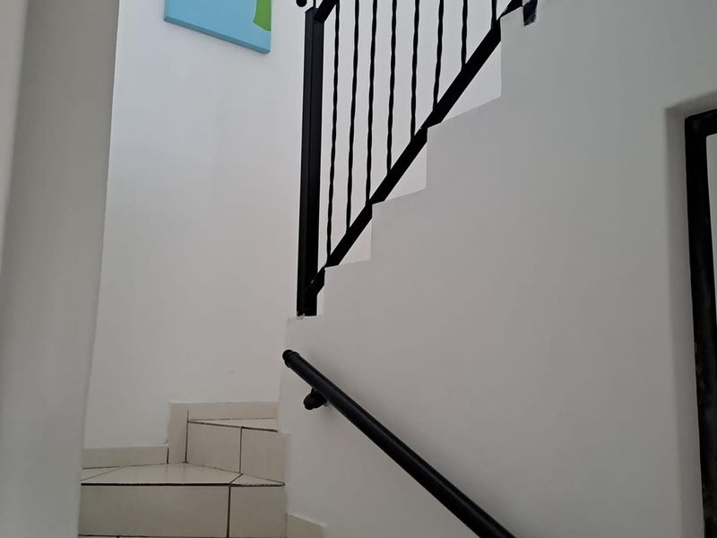 A clean, modern staircase featuring white tiled steps, a black metal balustrade, and a matching wall-mounted handrail.