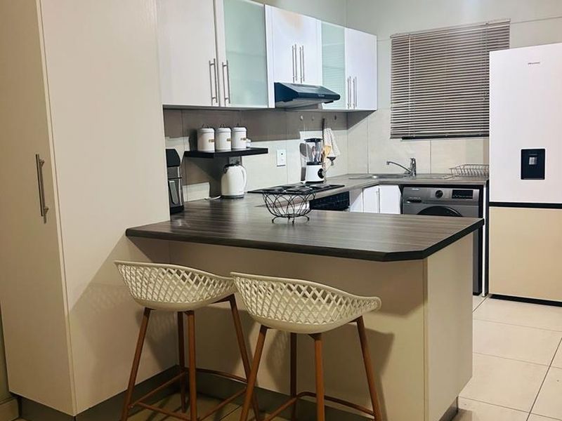 A functional kitchen featuring white cabinetry, a dark laminate breakfast bar, tiled flooring, and integrated fixtures including a sink and extractor fan.
