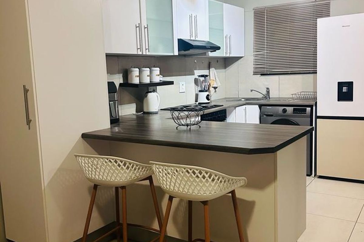 A functional kitchen featuring white cabinetry, a dark laminate breakfast bar, tiled flooring, and integrated fixtures including a sink and extractor fan.