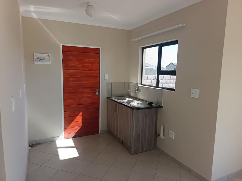 A compact kitchen area featuring tiled flooring, a single sink unit with built-in cabinetry, and a window providing natural light.