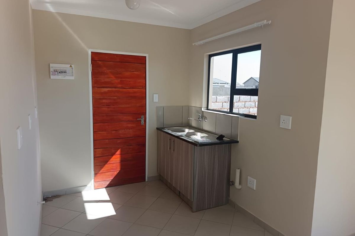 A compact kitchen area featuring tiled flooring, a single sink unit with built-in cabinetry, and a window providing natural light.