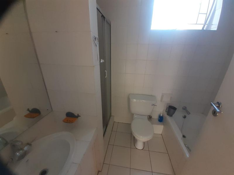 A functional bathroom featuring a shower enclosure, bathtub, toilet, and vanity basin with tiled walls and flooring, requiring some cosmetic updates.