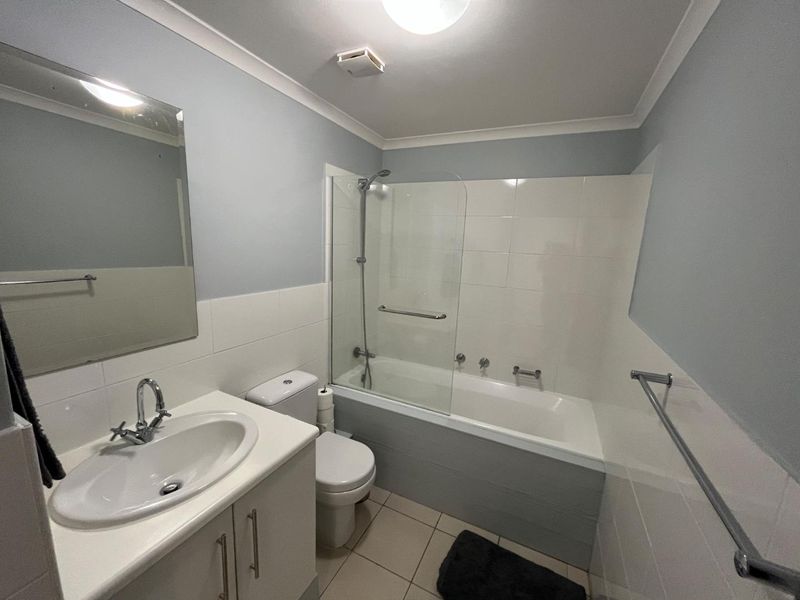 A clean and functional bathroom featuring a vanity with basin, a combined bathtub and shower with glass screen, and neutral wall tiling.