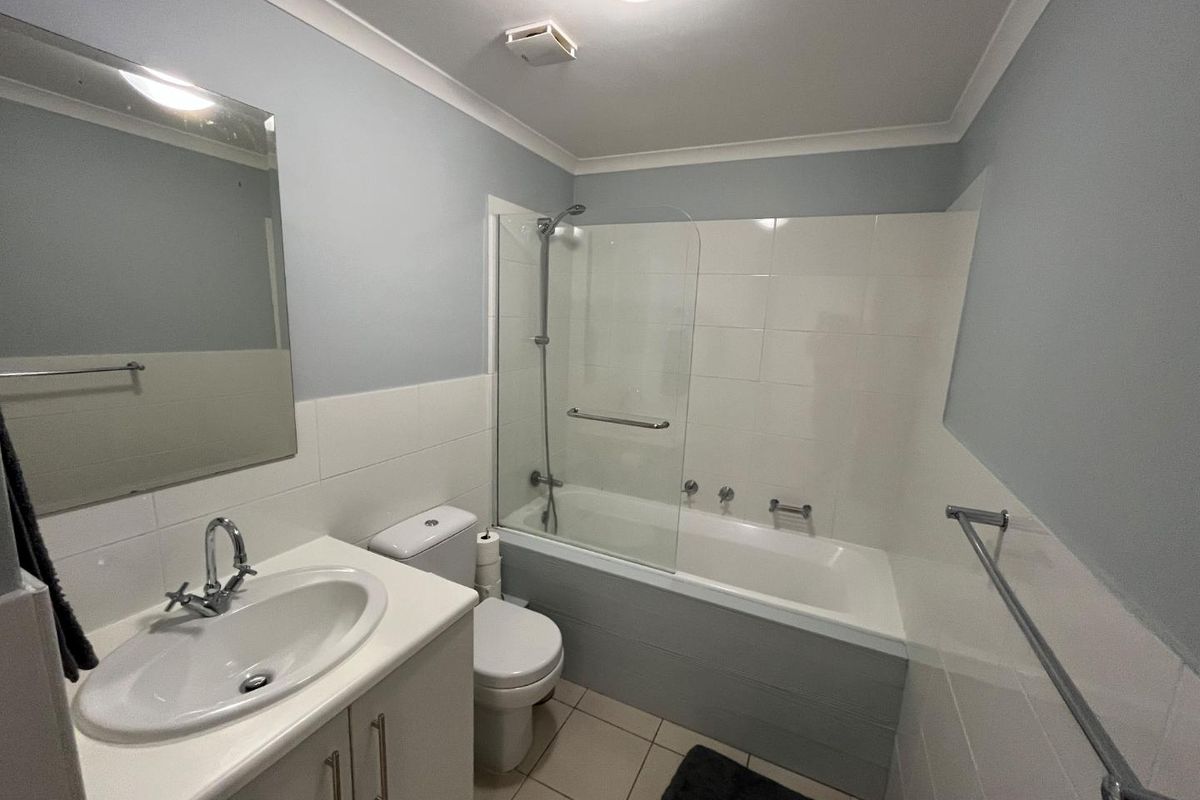 A clean and functional bathroom featuring a vanity with basin, a combined bathtub and shower with glass screen, and neutral wall tiling.