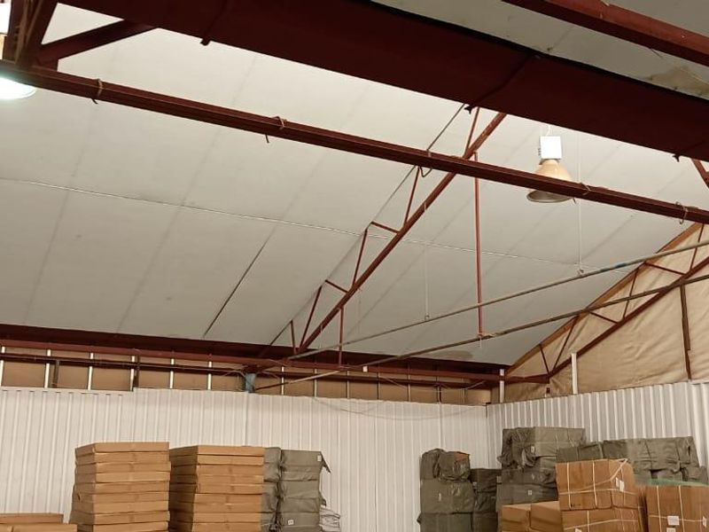 Spacious industrial warehouse interior featuring high pitched roof with exposed steel trusses, corrugated metal walls, and functional industrial lighting.