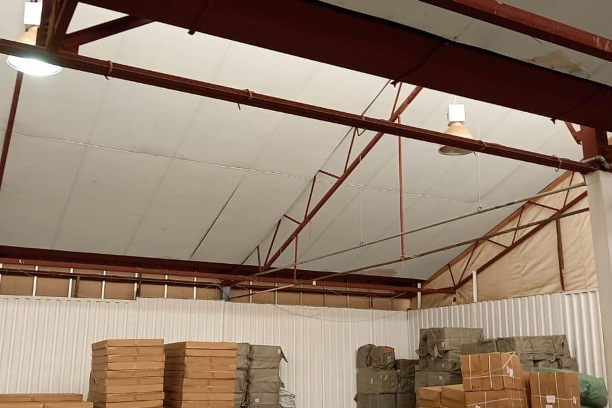 Spacious industrial warehouse interior featuring high pitched roof with exposed steel trusses, corrugated metal walls, and functional industrial lighting.