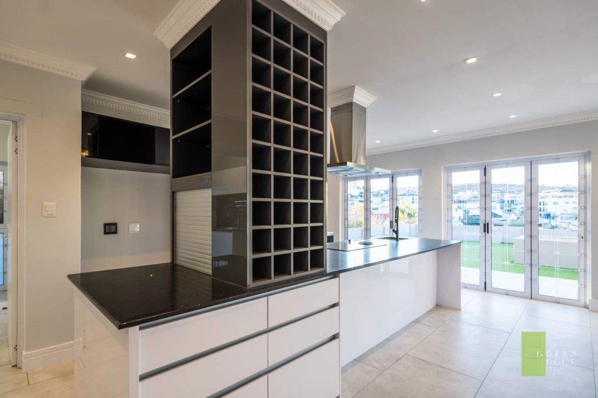 Modern kitchen featuring a central island with built-in wine rack, sleek cabinetry, stone countertops, stainless steel extractor fan, and direct access to the patio.