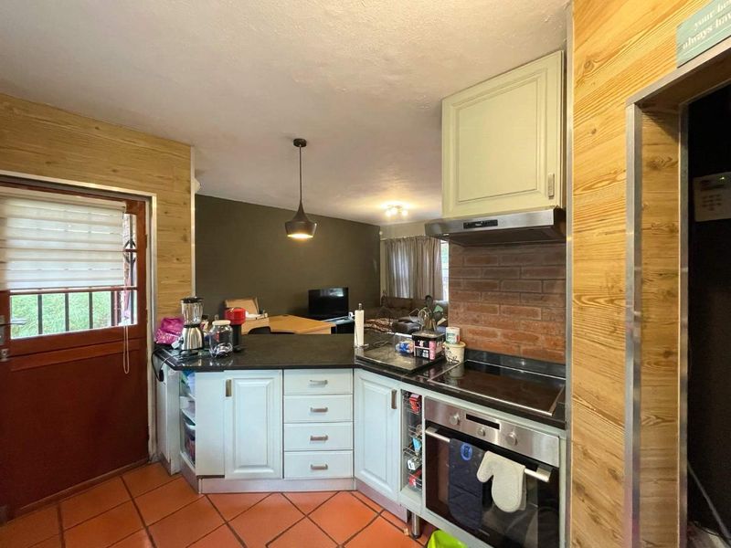 Open-plan kitchen and living area featuring built-in cabinetry, electric hob, oven, and terracotta flooring, offering a functional layout for modern living.