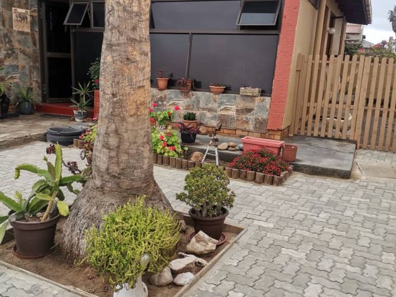 Rear exterior view featuring a paved courtyard area, stone wall accents, and a timber fence boundary.