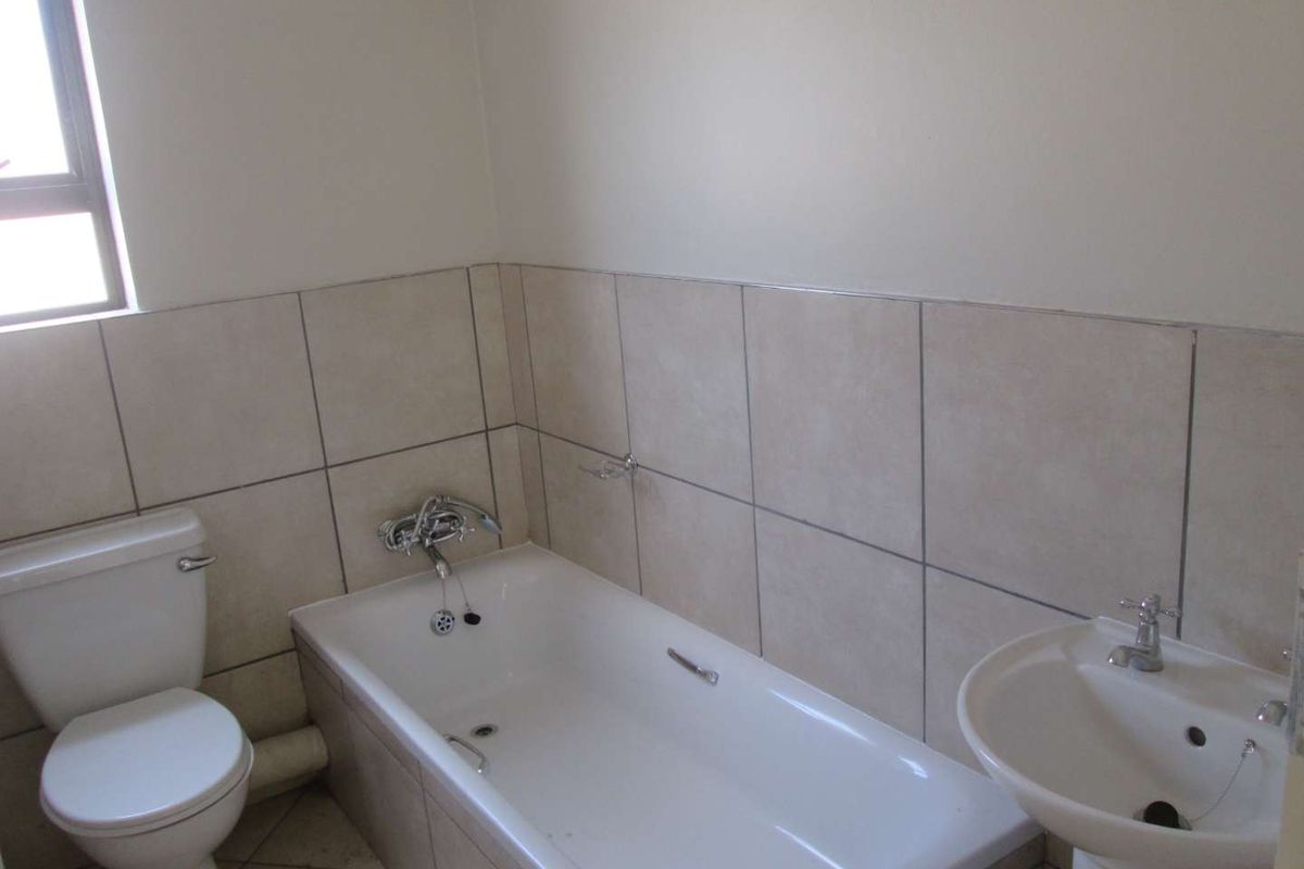 A functional bathroom featuring a bathtub, pedestal basin, and toilet with neutral wall and floor tiling.