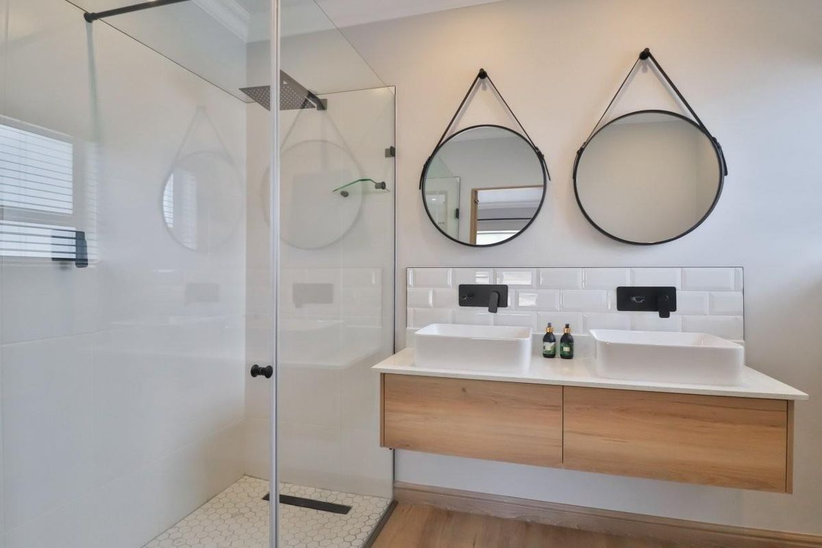 Modern bathroom featuring a floating double vanity with vessel sinks, wall-mounted matte black faucets, and a spacious walk-in shower with glass enclosure.