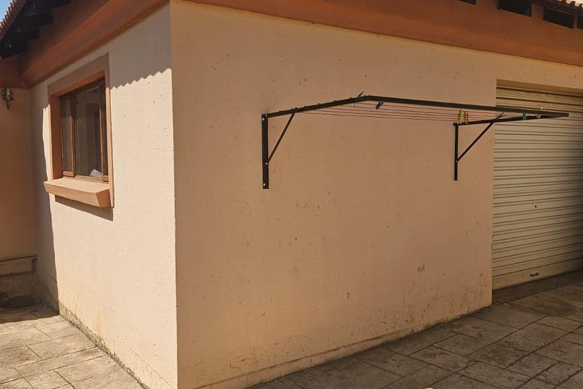 Rear exterior view of the townhouse featuring a paved patio area, a roller garage door, and a wall-mounted clothesline.