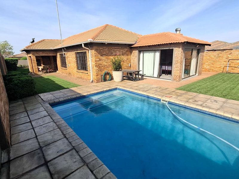 A well-maintained rear exterior view featuring a swimming pool with paved surround, brick house facade, and a manicured lawn area.