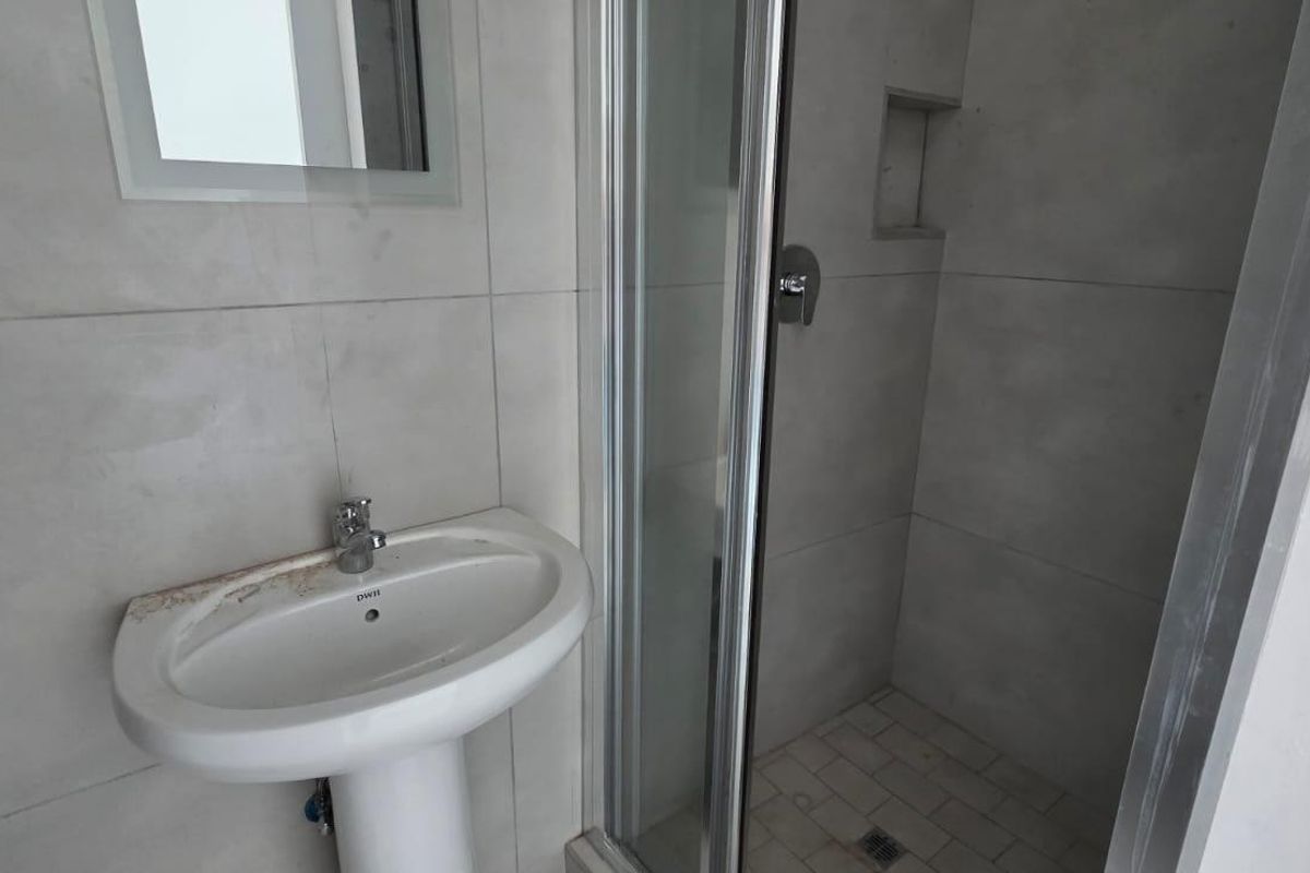 A compact bathroom featuring a pedestal basin, tiled walls, and a glass-enclosed shower with a built-in niche.