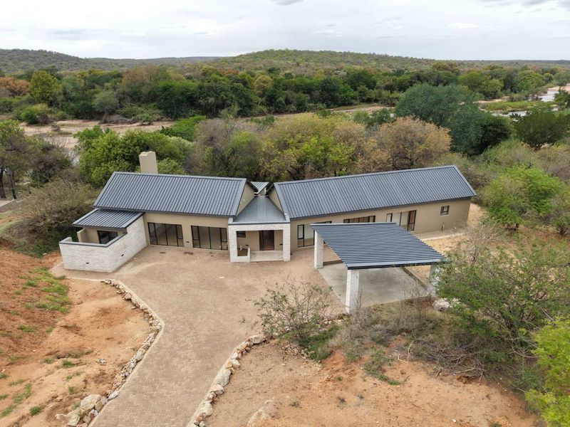 Aerial view of a modern single-story home featuring a metal roof, stone accents, and a paved driveway, set in a natural bushveld landscape.