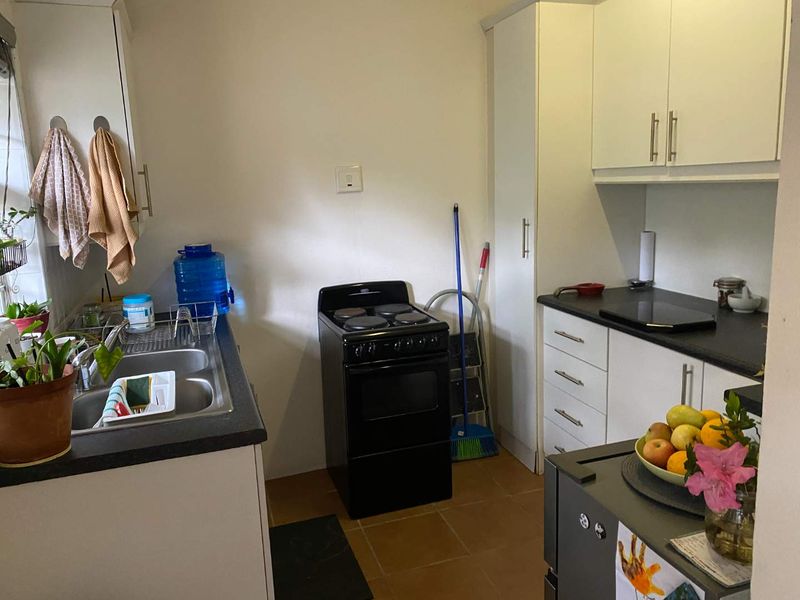 Compact kitchen featuring white cabinetry, dark laminate countertops, a double bowl sink, and a freestanding electric stove with tiled flooring.