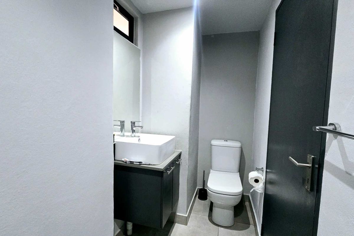 A modern, compact bathroom featuring a vanity with a basin, a toilet, and neutral floor tiling.