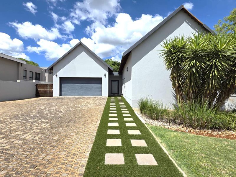 Modern front elevation featuring a paved driveway, double garage, and a well-maintained landscaped garden with a stepped pathway leading to the entrance.