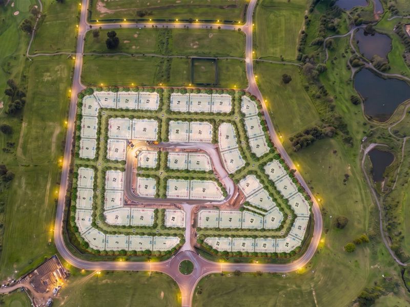Aerial view of a residential land development estate featuring numbered plots, paved internal roads, street lighting, and surrounding green space.
