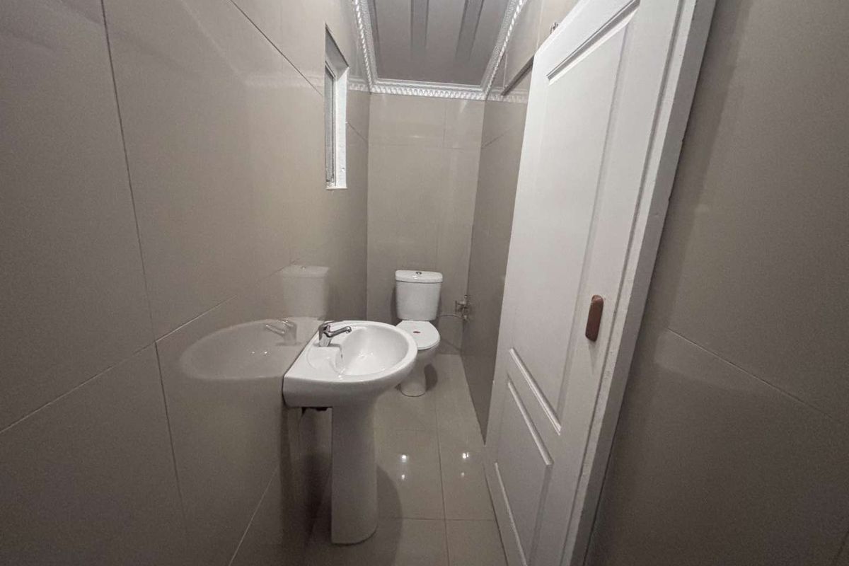 A compact bathroom featuring full-height wall tiling, a pedestal sink, and a standard toilet.