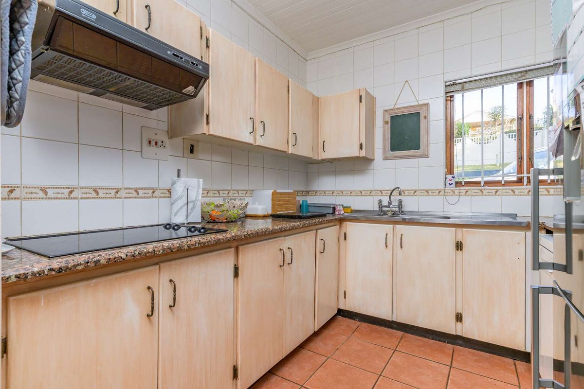 A functional kitchen featuring light wood-tone cabinetry, granite countertops, a built-in hob, extractor fan, and tiled flooring with a window overlooking the exterior.