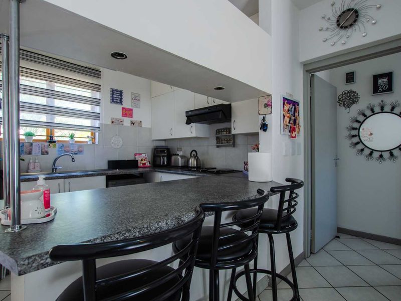 Compact kitchen featuring granite countertops, built-in cabinetry, an integrated extractor fan, and a functional breakfast bar area with tiled flooring.