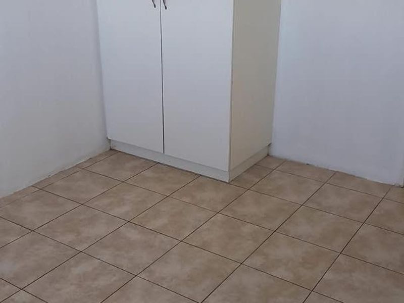 A simple, empty bedroom featuring neutral ceramic floor tiles and a white built-in wardrobe.