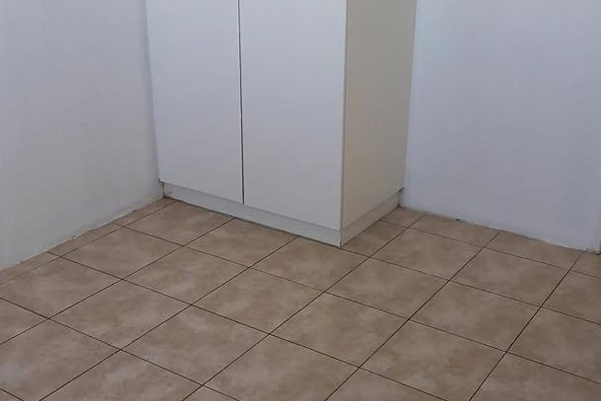 A simple, empty bedroom featuring neutral ceramic floor tiles and a white built-in wardrobe.