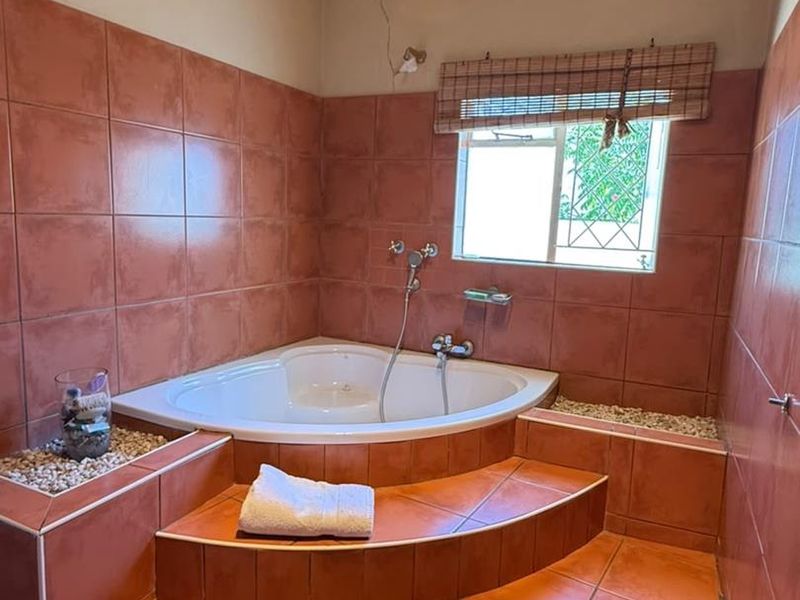 Bathroom featuring a raised corner bathtub with tiled steps and ceramic wall tiling, requiring some maintenance to address visible wall cracking.