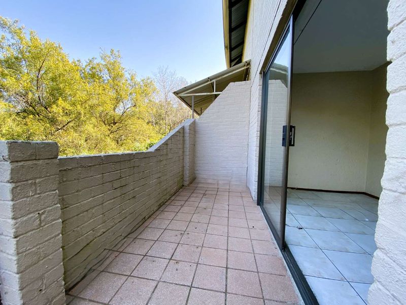 A private balcony featuring tiled flooring, a brick parapet wall, and a sliding glass door providing access to the interior living space.
