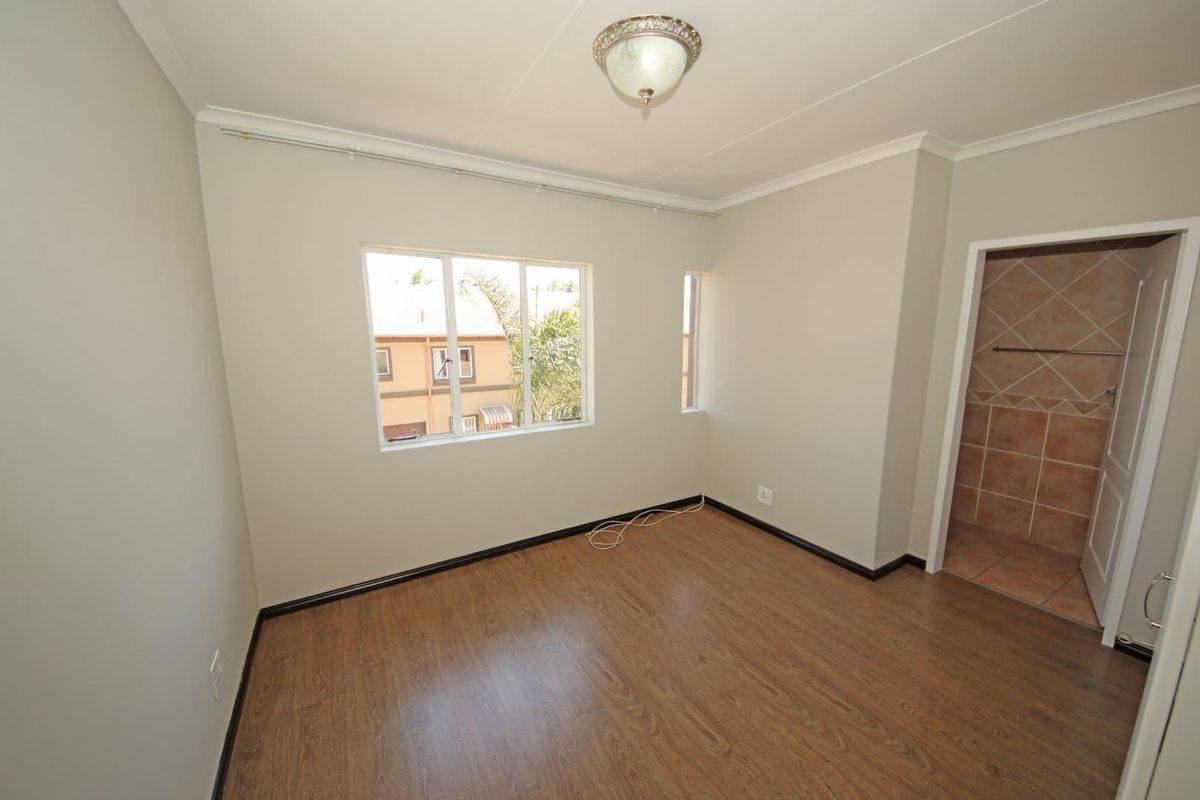 A bright, empty bedroom featuring wood-look laminate flooring, neutral wall paint, and an adjoining tiled bathroom area.