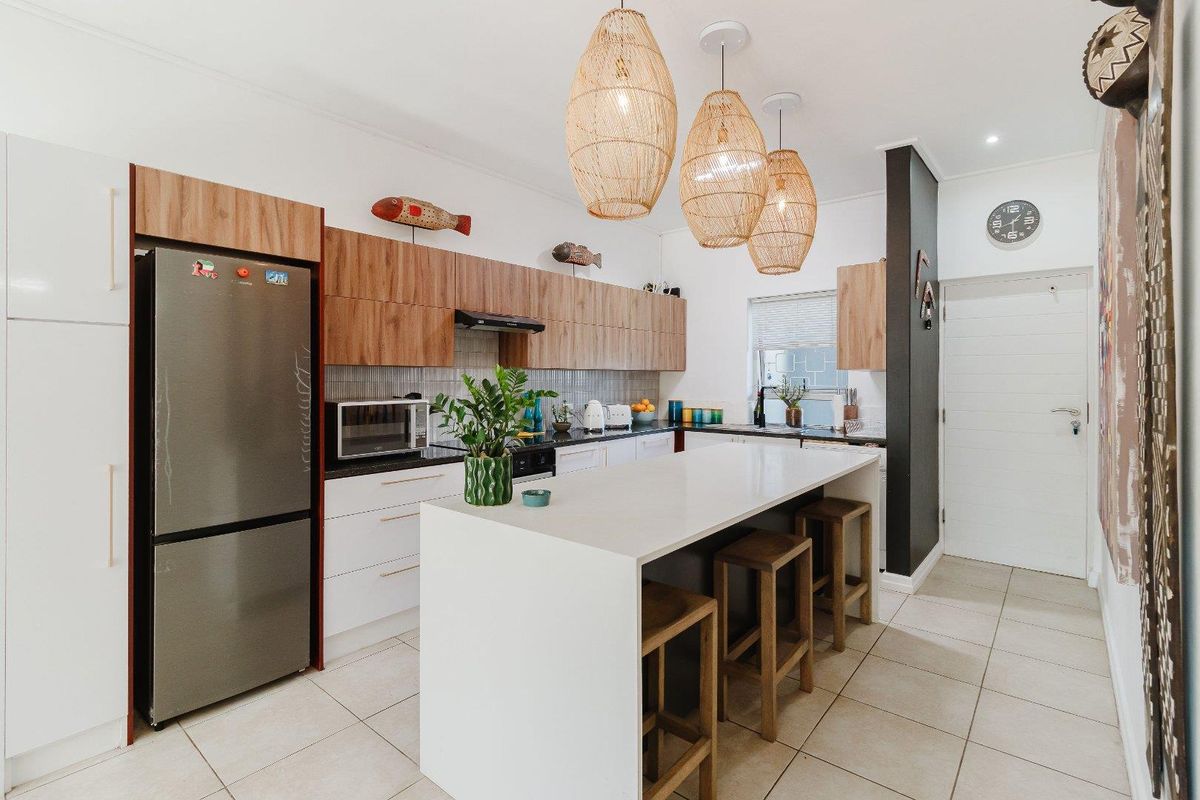 Modern kitchen featuring a central island with breakfast bar seating, sleek cabinetry, stone countertops, and tiled flooring in an open-plan layout.