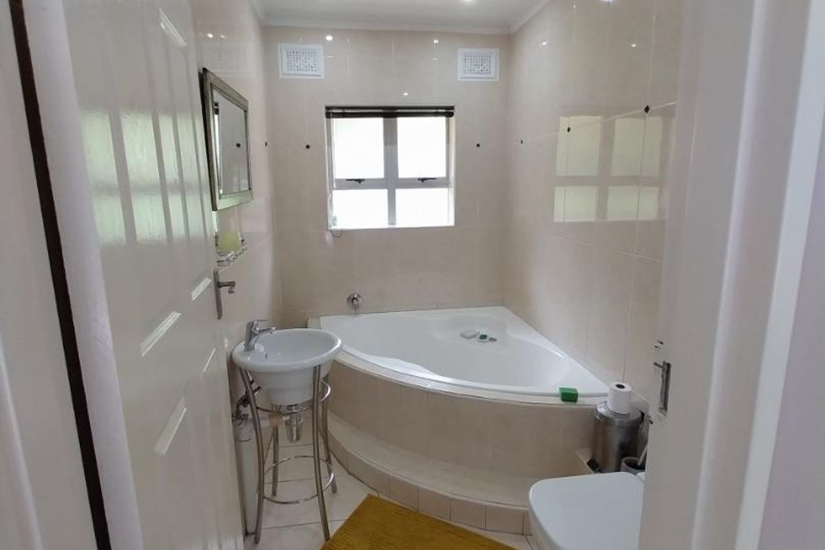 A compact bathroom featuring a corner bathtub, pedestal basin, toilet, and neutral tiled finishes with recessed lighting.