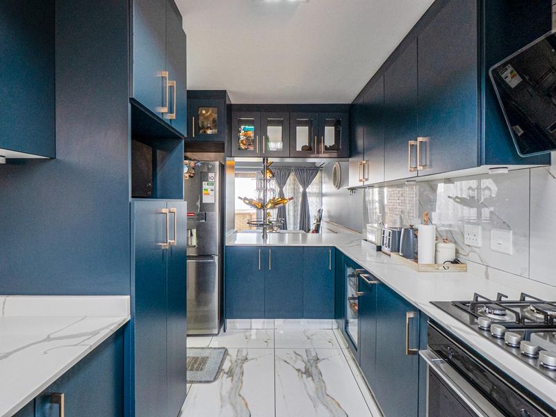 Modern galley-style kitchen featuring navy blue cabinetry, marble-look quartz countertops, high-end built-in appliances, and elegant marble-look floor tiles.