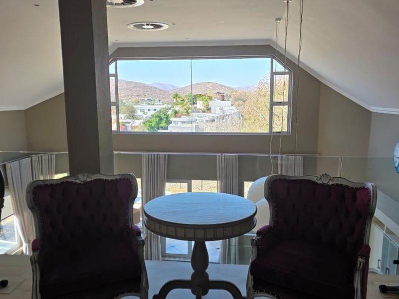 A bright living area featuring a glass balustrade, recessed lighting, and a large picture window offering scenic views.