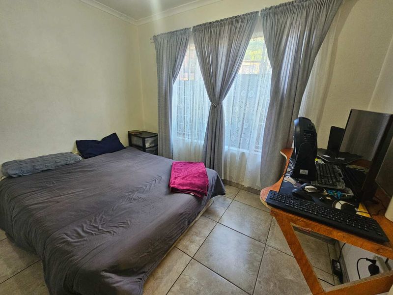 A functional bedroom featuring tiled flooring and large windows with installed curtain rails, providing a neutral space ready for personalization.