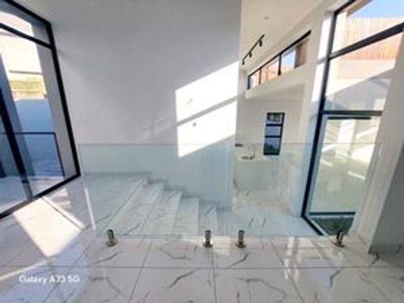 Modern entrance hallway featuring high-quality marble-look floor tiles, a sleek glass balustrade, and expansive windows that provide abundant natural light.