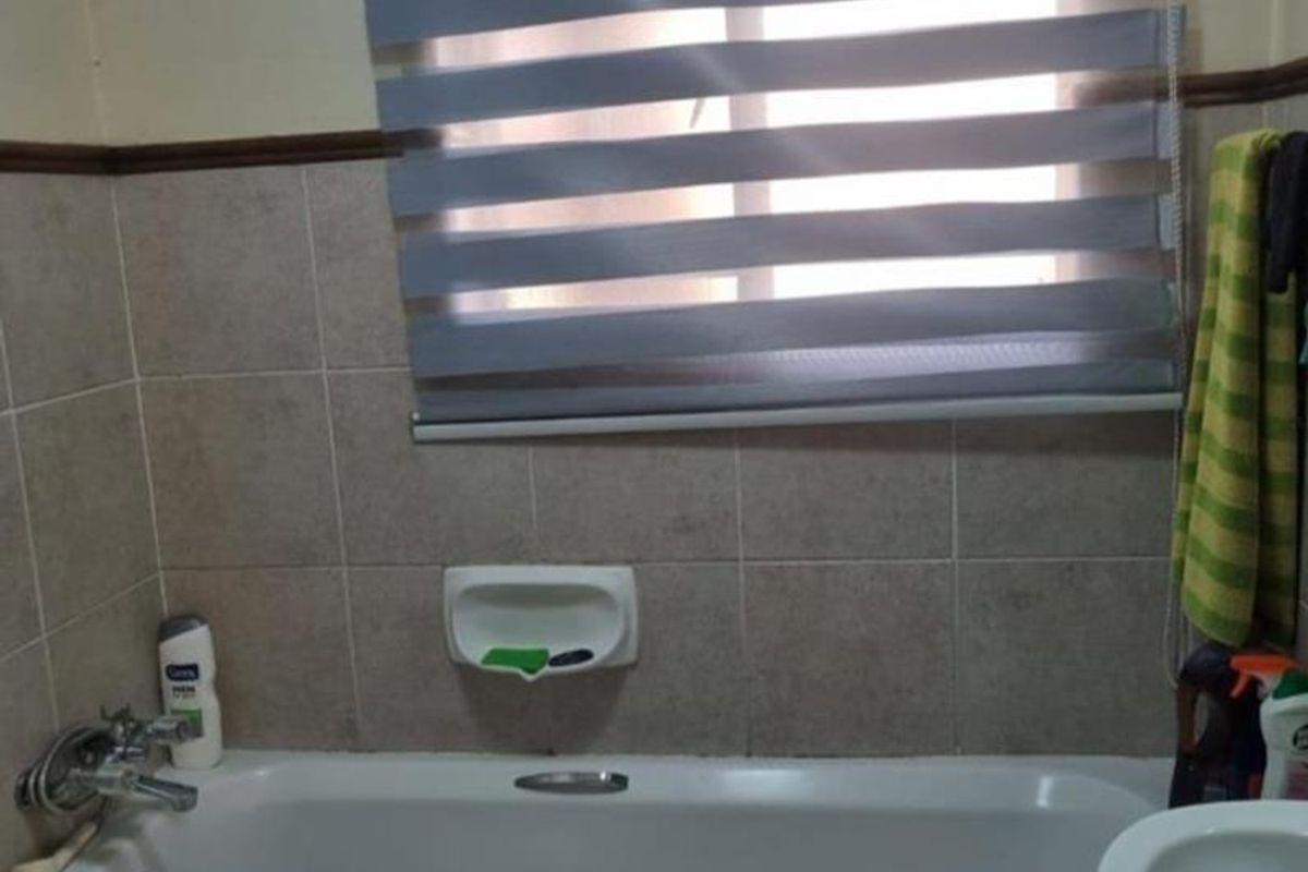 A functional bathroom featuring a bathtub with tiled surround, built-in soap dish, and a window with a modern roller blind.