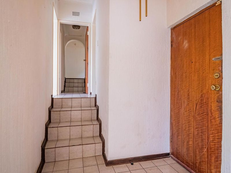 A functional hallway featuring tiled flooring and a short staircase leading to an inner passage, with a solid wooden door at the entrance.