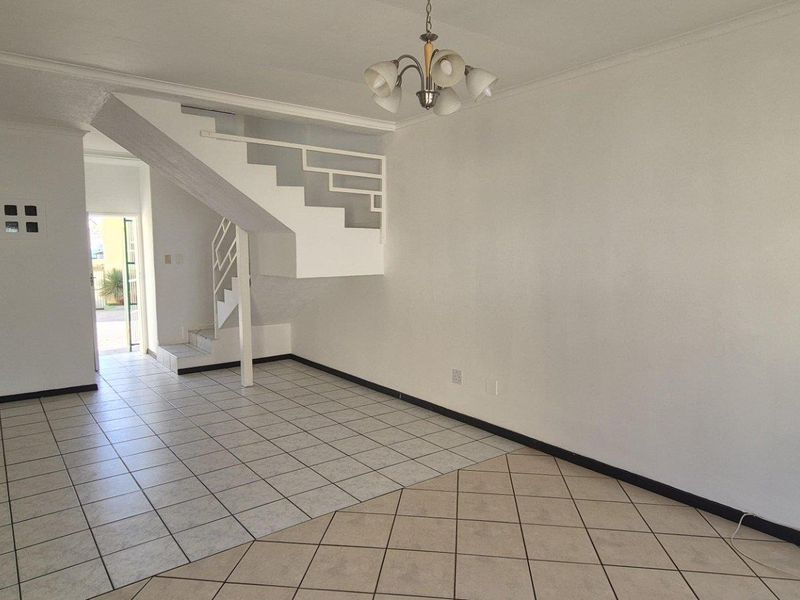 An open-plan living area featuring a staircase, tiled flooring throughout, and a neutral color palette, offering a blank canvas for interior design.